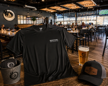 A black DESTIHL short-sleeve athletic T-shirt is displayed on a wooden table in a restaurant setting