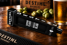 DESTIHL Brewery tap handle on a wooden surface with hops and a glass of beer in the background.