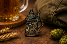 Decorative beer mug pin on a wooden surface with a glass of beer and hops.