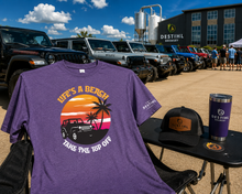A purple DESTIHL Brewery branded t-shirt with a beach sunset graphic is displayed in an outdoor event 