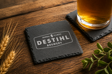 Coaster with DESTIHL Brewery logo on a wooden surface with a glass of beer and wheat stalks.